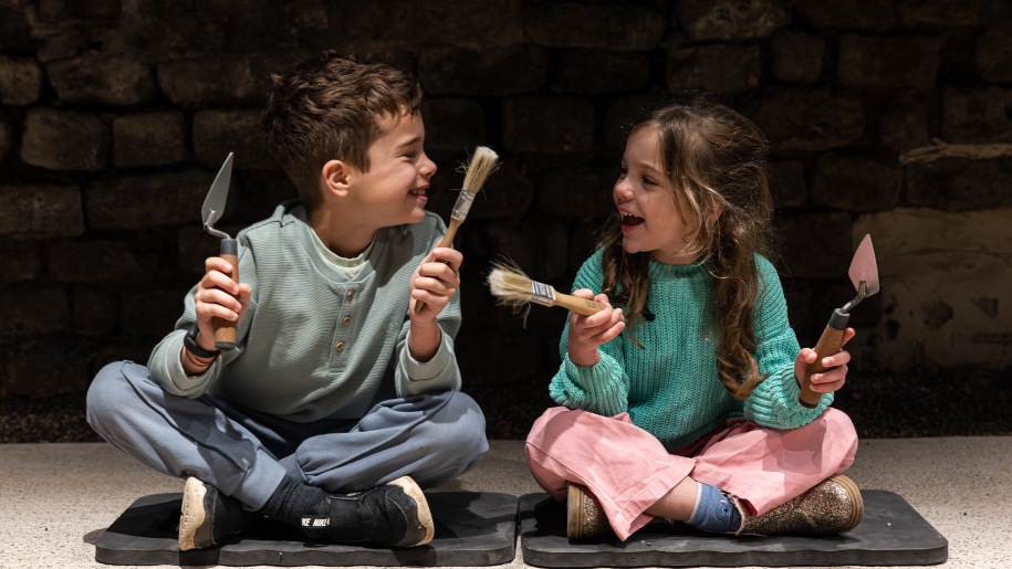 Two children holding archaeologists' trowels and brushes.