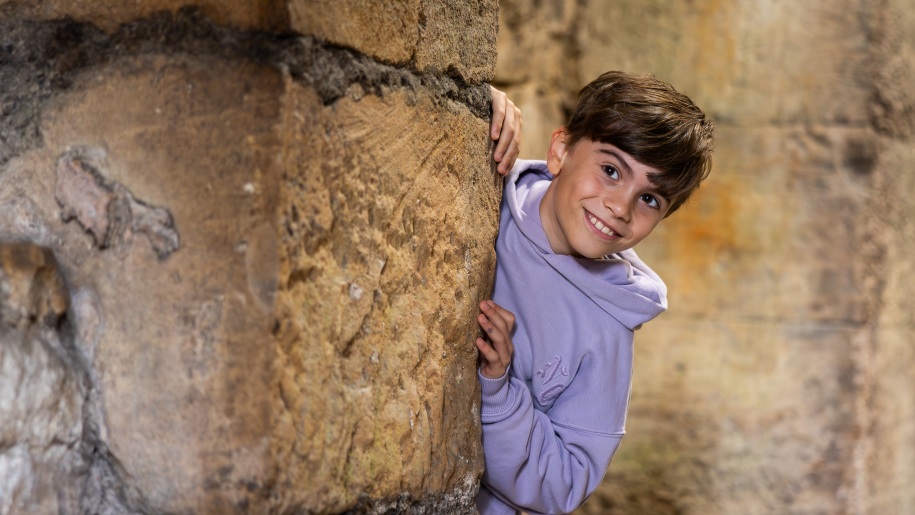 A boy peeping out from behind a stone pillar.