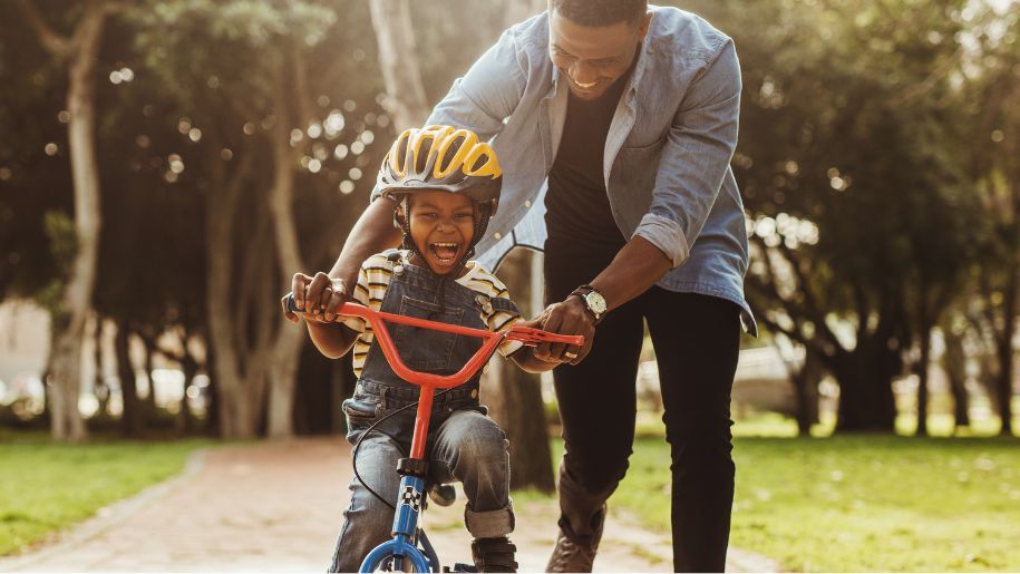 boy being pushed on his bike in a park by a father