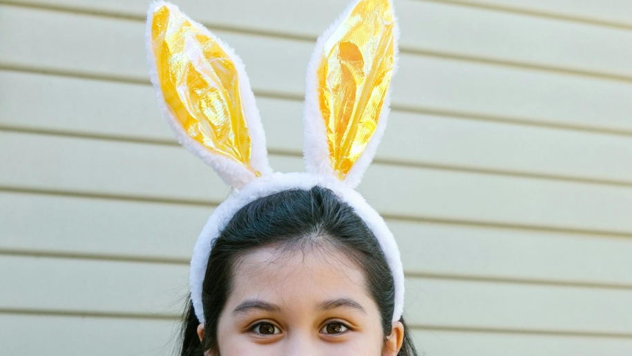 Girl wearing gold bunny ears on a white headband.