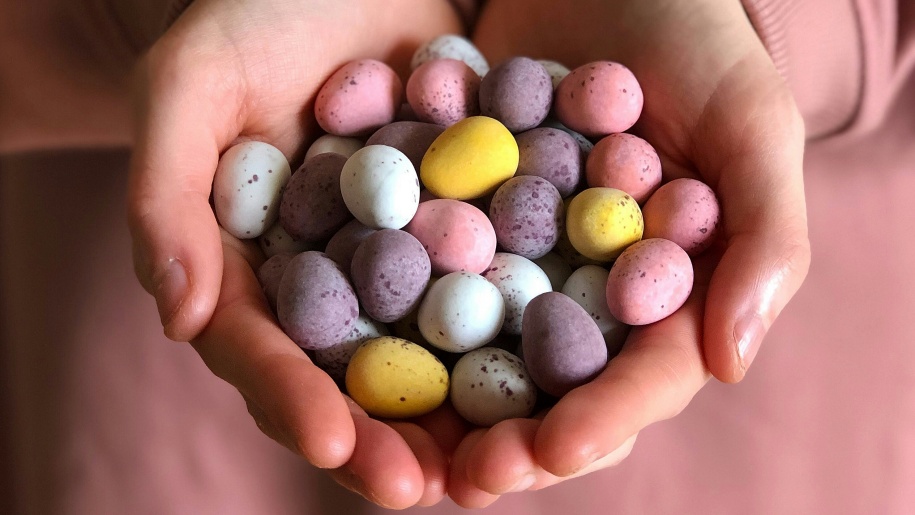 A person's hands holding a heap of small coloured chocolate Easter eggs.