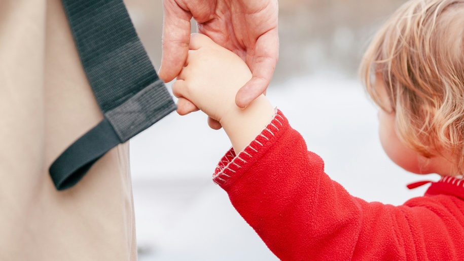 Toddler in a red jersey holding an adult's hand.