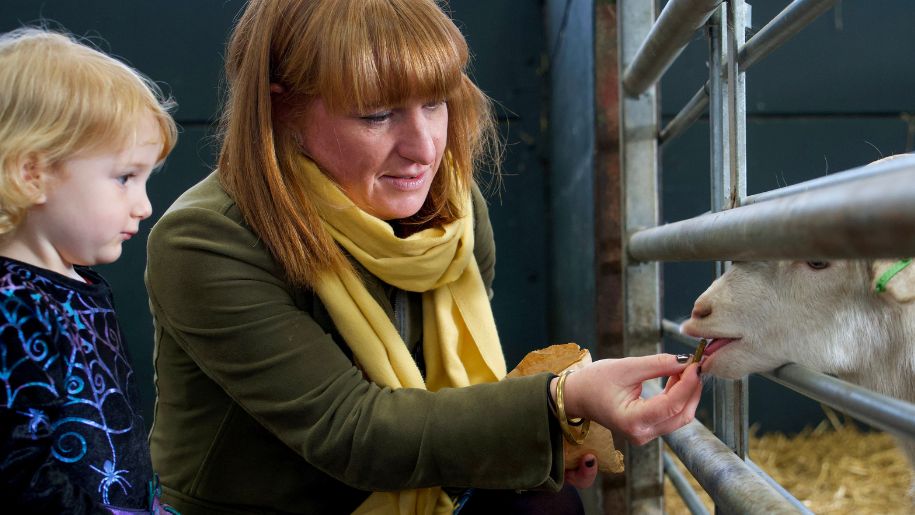 Mum feeds a lamb as little girl watches