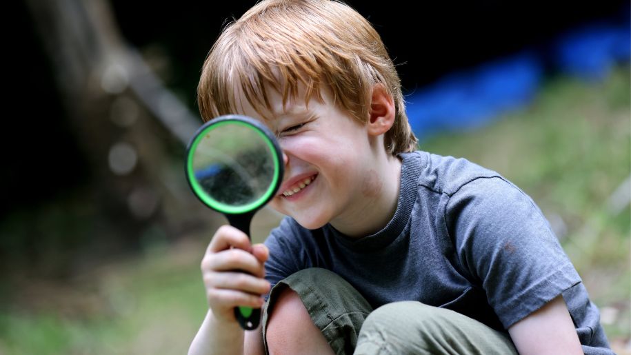 brown haired boy looks through green magnifying glass