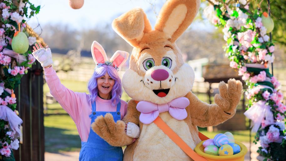young lady in purple wig and bunny ears smiles and waves next to a person dressed in a brown bunny costume