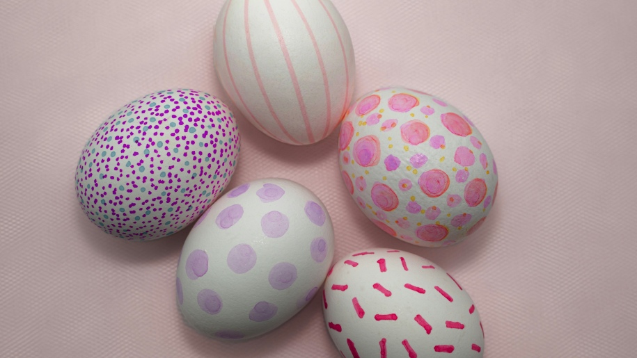 Five Easter eggs decorated in pink and mauve against a pink background.
