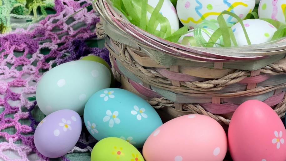 Easter eggs painted in pastel colours in and beside a wicker basket.