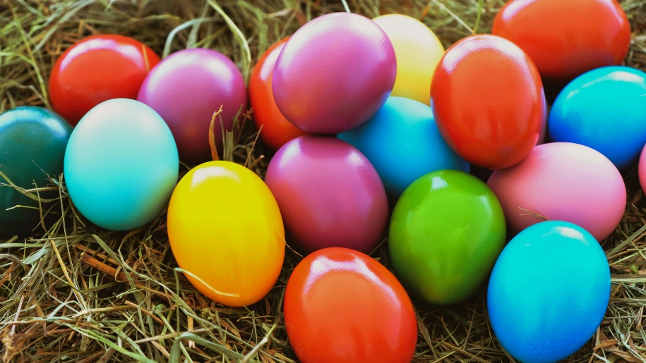 Pile of brightly painted Easter eggs on grass.