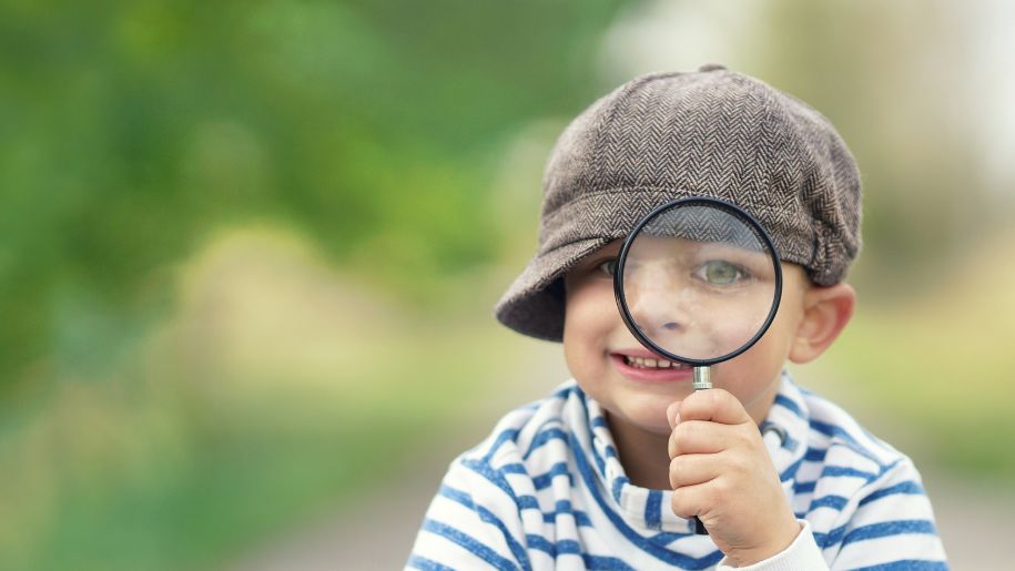 boy with hat and magnifying glass smile at camera