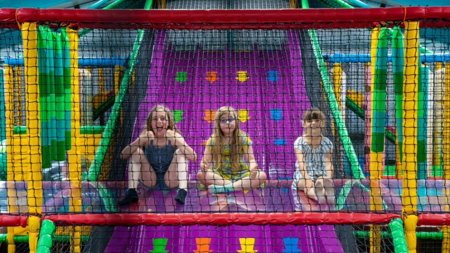 three children sit at the top of a colourful soft play