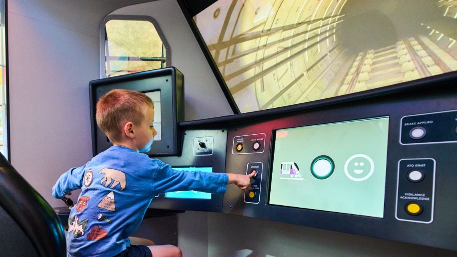 little boy in blue jumper sits at a control panel for a train or plane