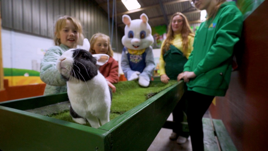 The Easter Bunny and a group of children looking at a black and white rabbit on a table.