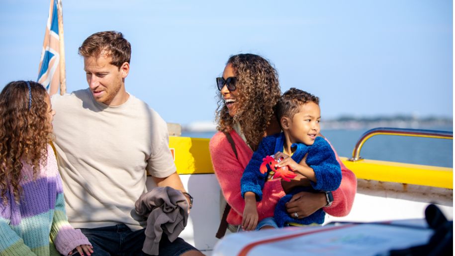 family of mother and father and two children sit on a yellow boat with a UK flag behind them