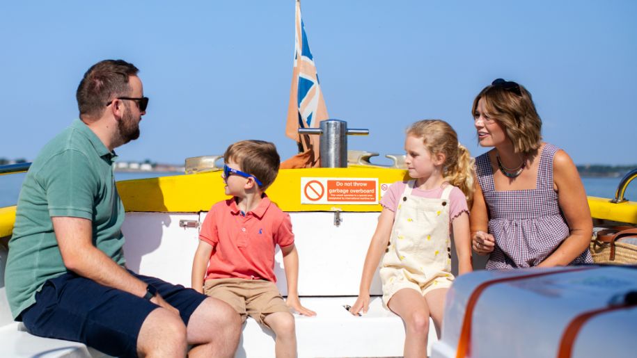 family sit on a yellow boat, mother, father and boy and girl with blue sky behind them