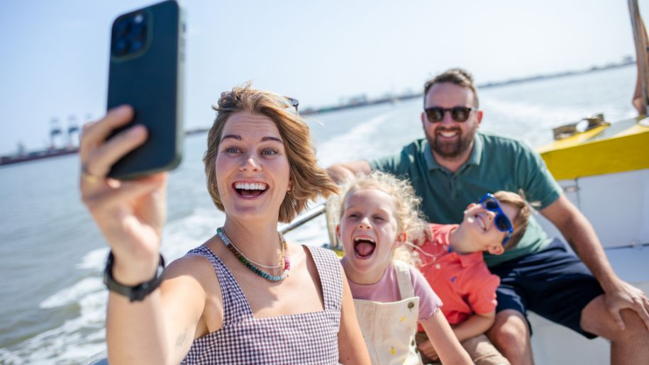family pose for a photo on an iphone as they speed along on a yellow boat