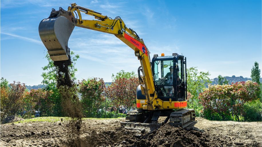 yellow digger on pile of dirt infront of blue sky