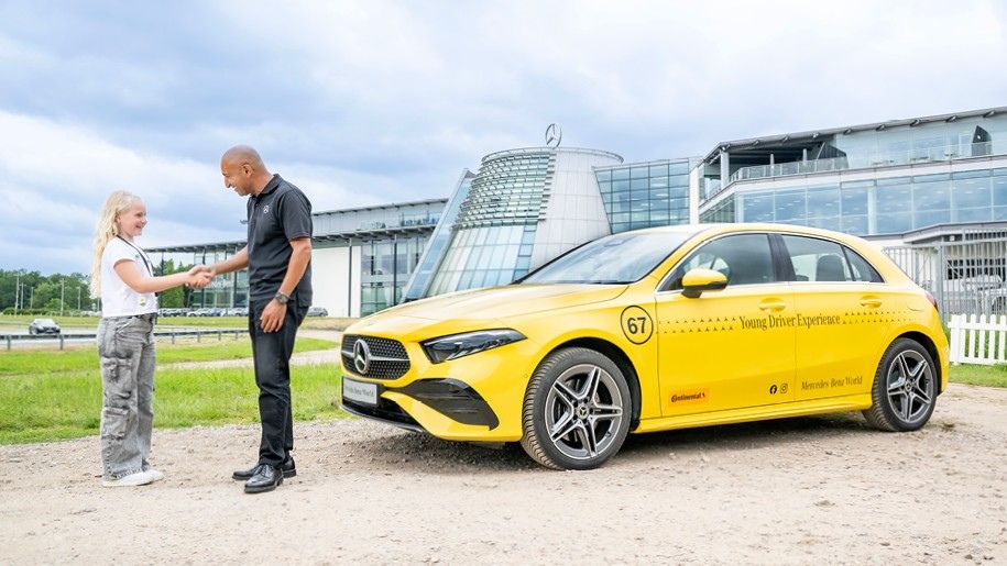 girl shakes the hand of a mercedes benz employer infront of a yellow car