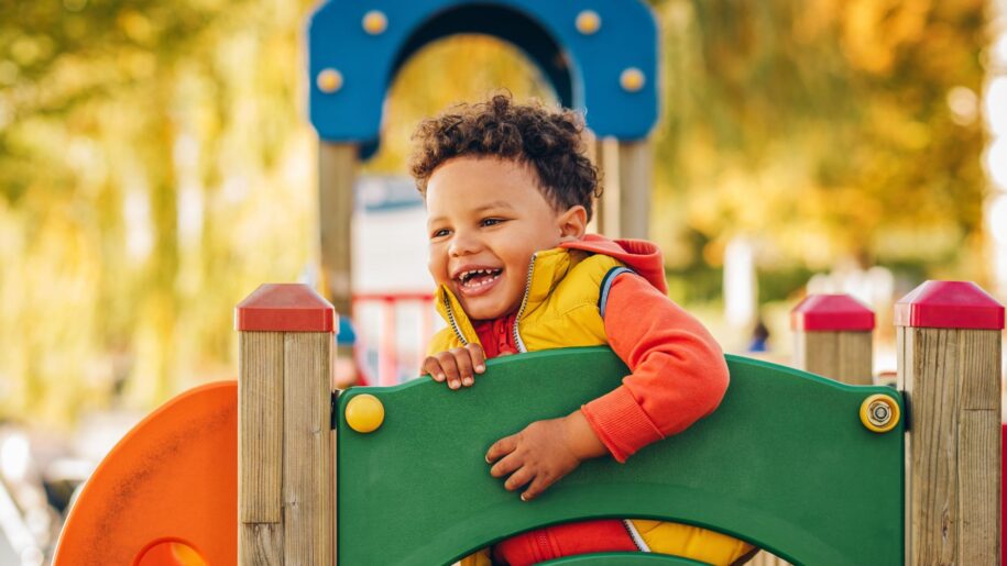 Adorable little 1-2 year old toddler boy having fun on playground, child wearing orange hoody jacket and yellow vest