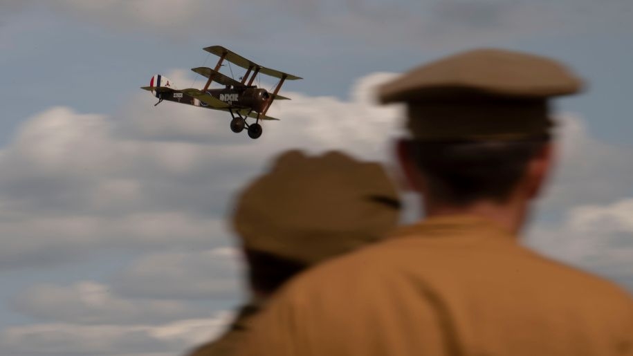 Men in military uniform watching a triplane in the sky.