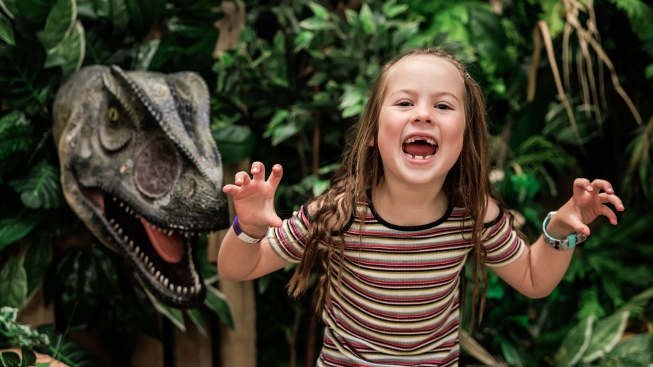 Young girl roaring beside a large model dinosaur.