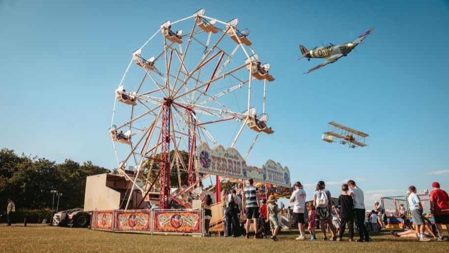 ferris wheel against a blue sky with an aeroplane midflight above it