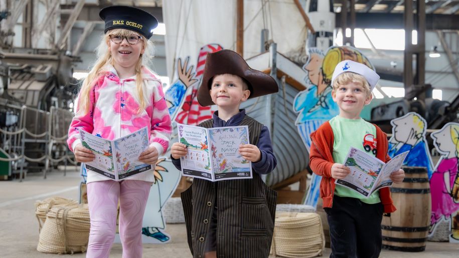 three children stand with leaflets and sailor hats