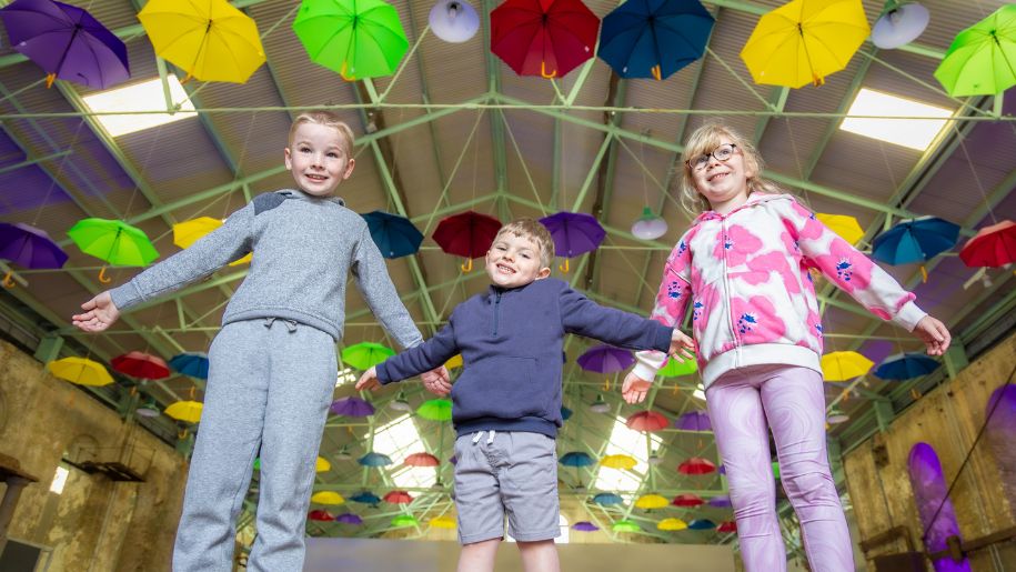 three children look down at camera with multicoloured umbrellas behind them