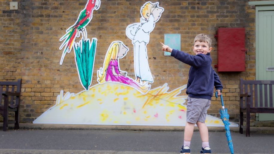 boy holding a blue umbrella looks at illustrations on the wall