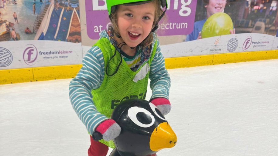 little girl on ice rink with a penguin holder