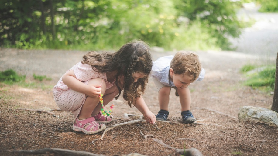 Two children watching something on the ground amongst tree roots.