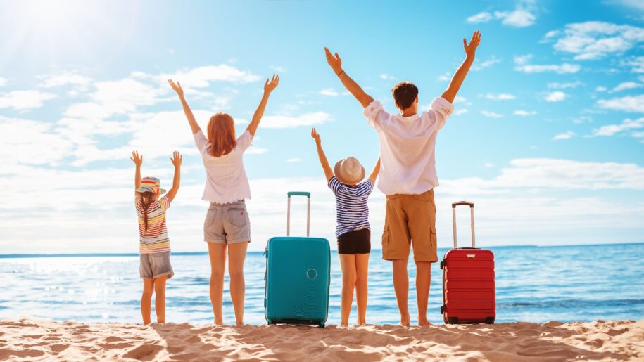 family stand on beach with suitcases