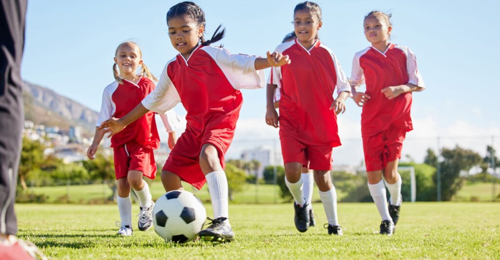 girls in red football strips playing with a black and white ball