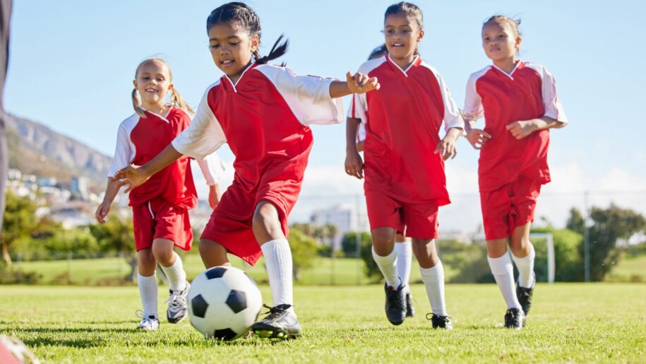 girls in red football strips playing with a black and white ball