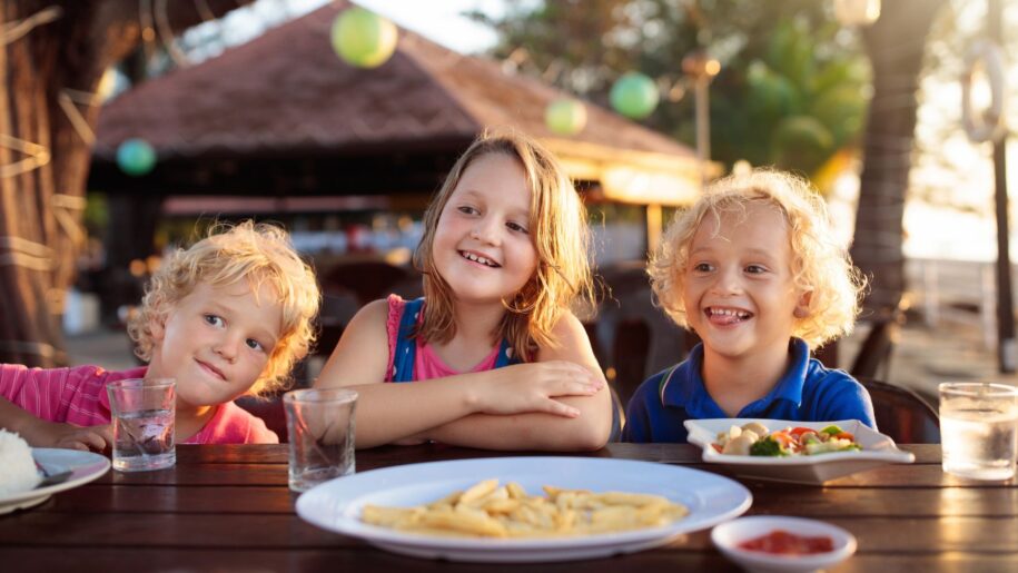 three children sit outside in the summer eating dinner