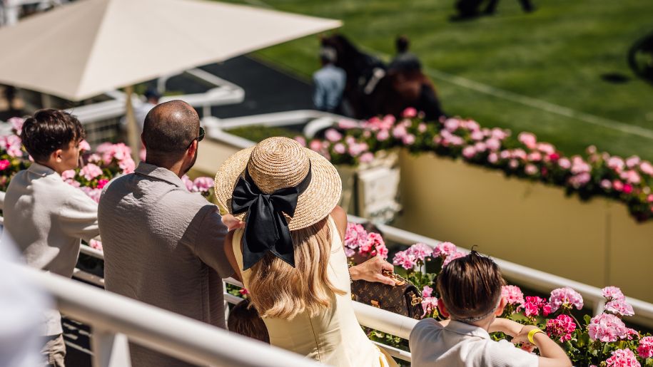 girl holds on to summer straw hat with black bow while watching the racing