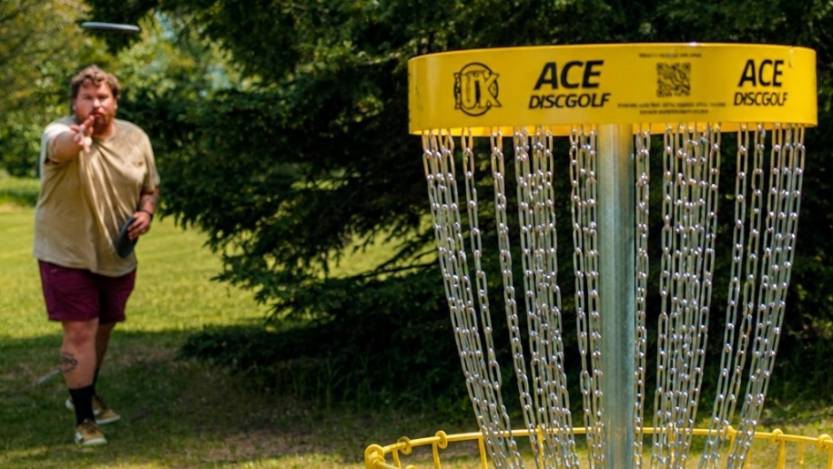 A man throwing a disc into the basket during a game of disc golf.