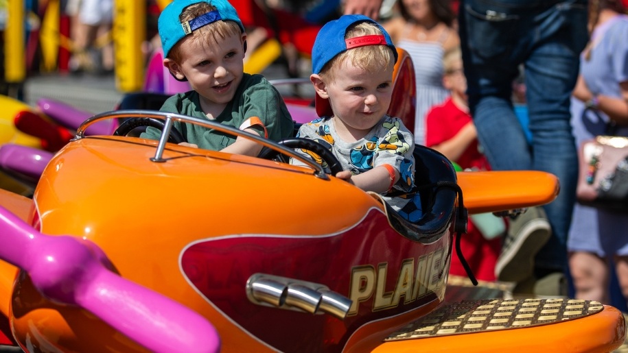 Two young boys sitting in an orange plane on a funfair ride.