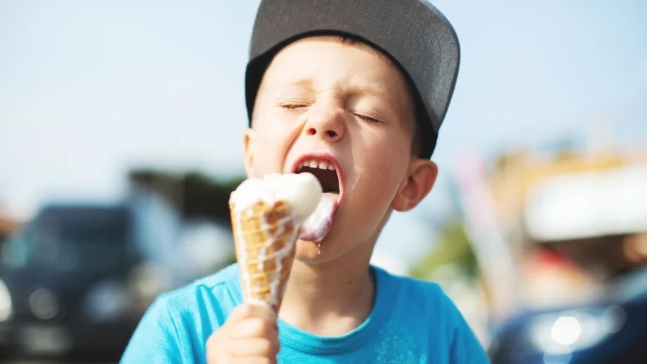 Boy in a cap licking an ice cream cone.