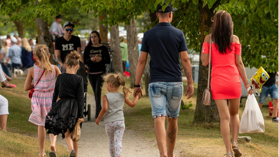 Family of five walking along a path in a crowded green space.