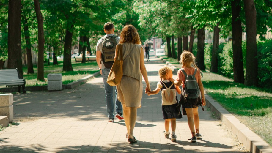 Family of four walking through a park in sunshine.