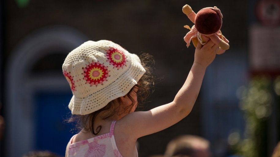 Young girl wearing a crocheted sun hat holding up a toy.