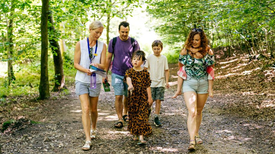 Adults and children walking along a woodland path in summer.