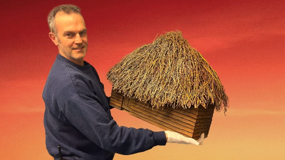 A man holding a model of a thatched hut.