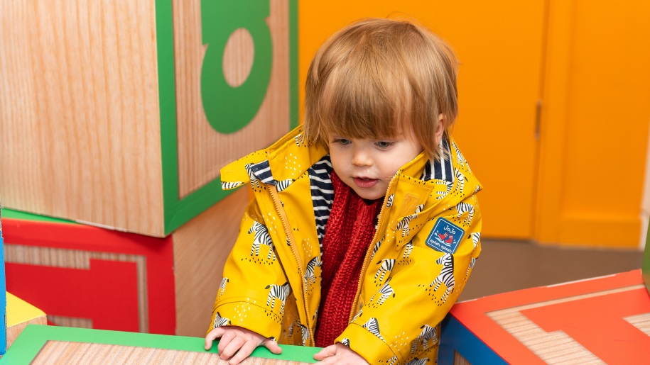 A toddler in a yellow jacket standing at an activity table.