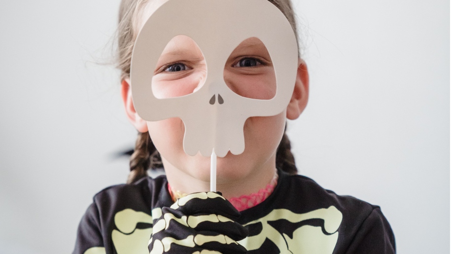 Girl in skeleton fancy dress costume holding a skull mask in front of her face.