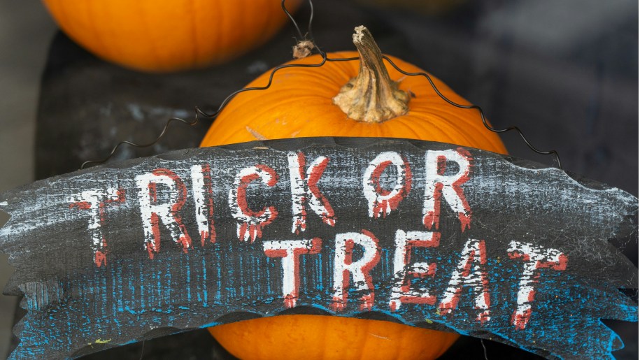 Trick or treat sign propped up against an orange pumpkin.