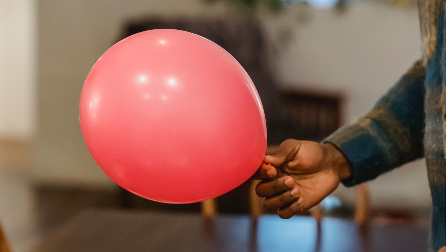 A hand holding a red party balloon.