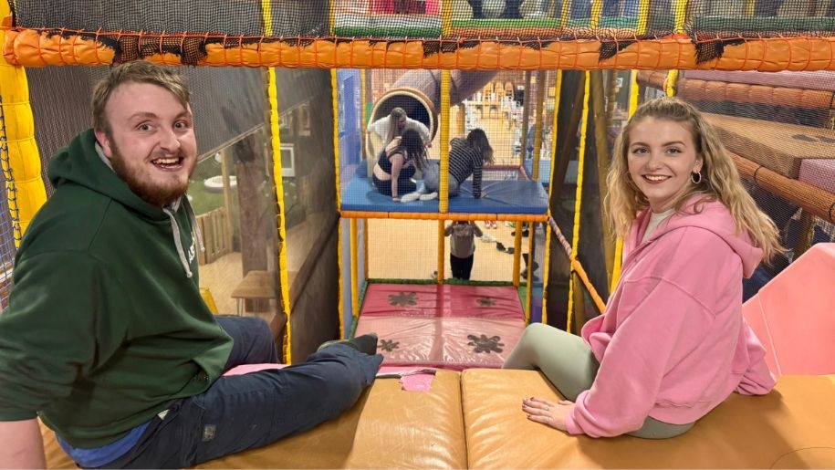 A man and a woman about to go down a slide at an indoor playbarn.