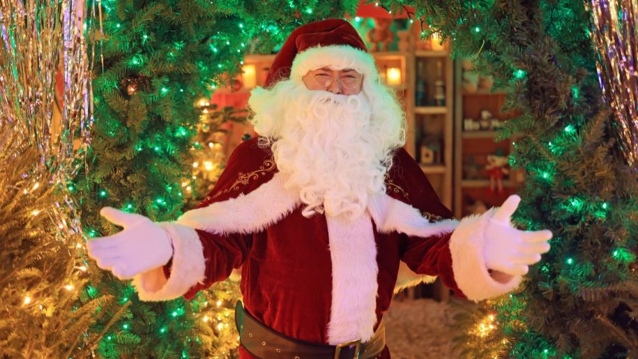 Father Christmas in red and white outfit in front of the entrance to his grotto.