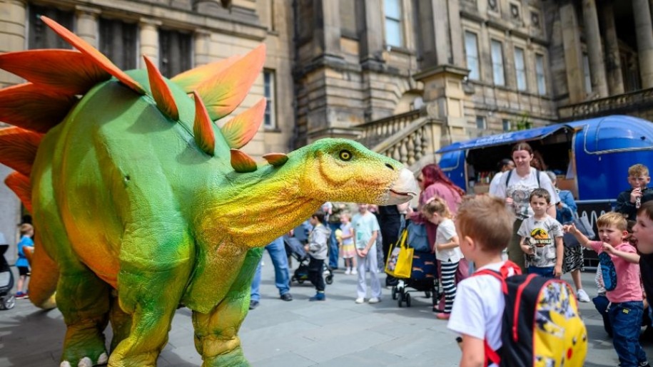 A boy looking at a model of a green and yellow dinosaur outside the World Museum Liverpool.